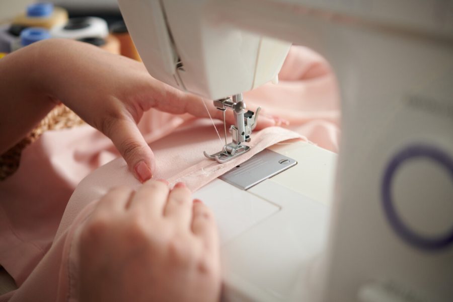 Close-up image of seamstress sewing silk dress for customer